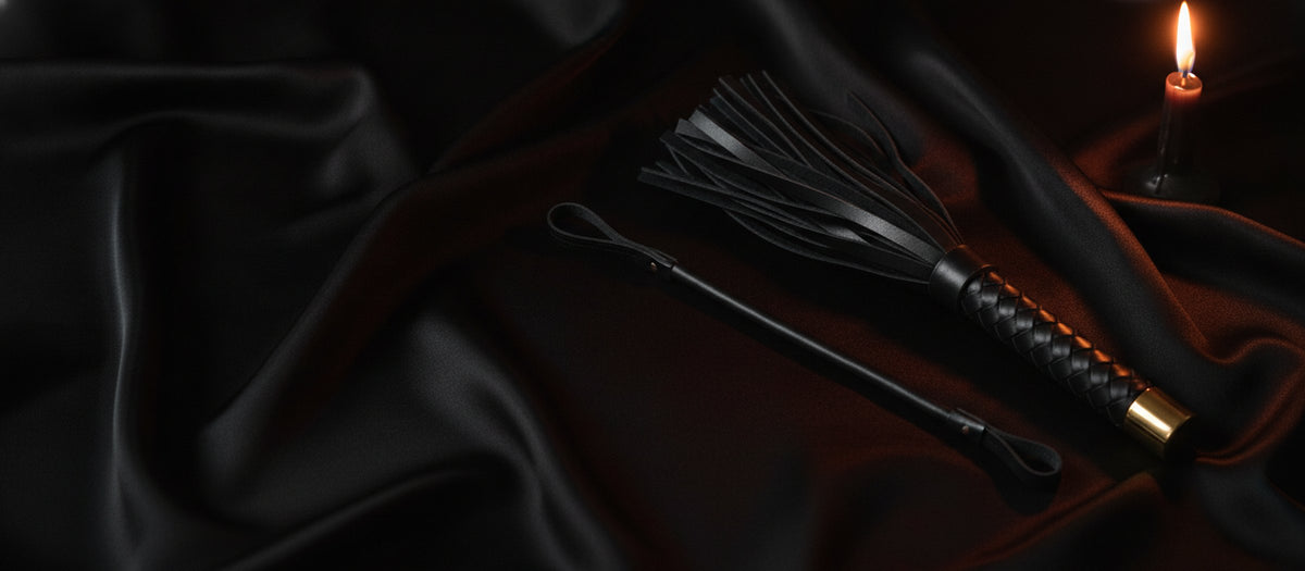 Leather flogger and riding crop on black satin sheets